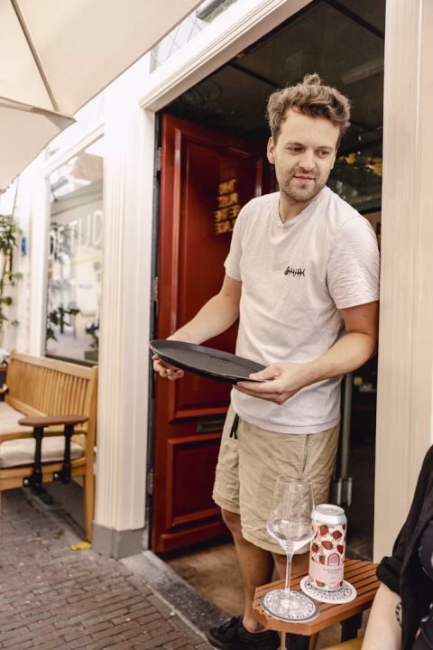Server standing in the doorway holding an empty serving tray at the café entrance
